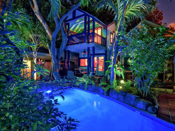 Luxurious tropical treehouse with a glowing blue pool, lush greenery, and ambient lighting at night.