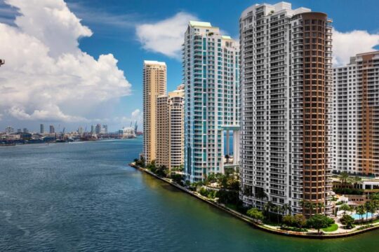 Miami waterfront skyline with modern high-rise condominiums overlooking the blue ocean under a cloudy sky.