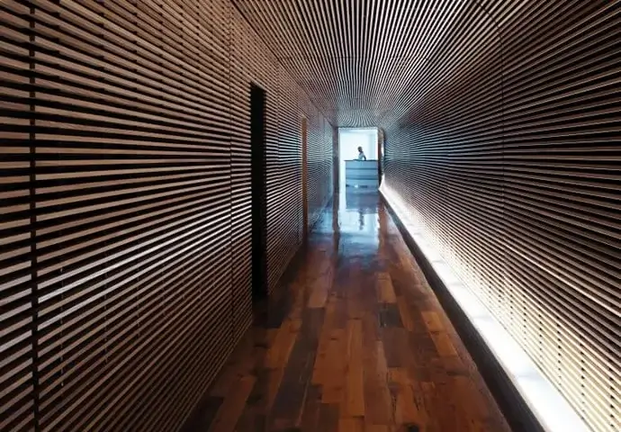 Wooden-slat hallway with polished floor leading to a bright room where a person stands at a counter at Standard Hotel Miami Beach