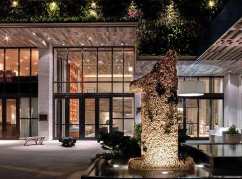 Modern luxury hotel entrance at night, featuring a large, textured "1" sculpture illuminated by warm light, lush vertical gardens, and contemporary architecture with glass and wood accents.
