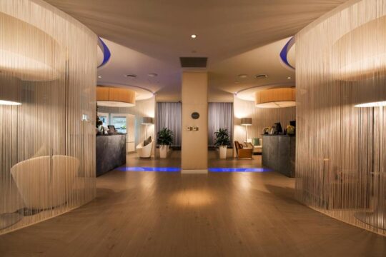 Luxurious hotel lobby with modern design, featuring sheer white curtains, ambient blue lighting, and sleek reception desks.