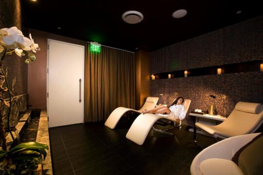 Relaxing spa lounge with a woman reclining on a chaise lounge, orchids, and an illuminated exit sign.
