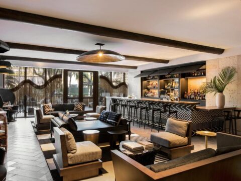 Stylish hotel lounge with a modern bar, plush seating, and tropical decor. Features dark wood beams, patterned upholstery, and a vibrant atmosphere perfect for relaxation.