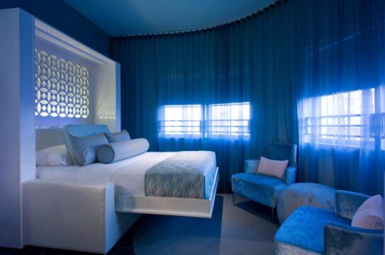 A modern, luxurious bedroom with a large, comfortable bed and plush blue seating. The room features elegant blue curtains and soft, ambient lighting, creating a serene and inviting atmosphere.
