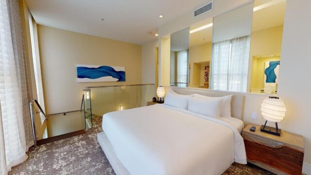 A luxurious hotel suite bedroom with a king-size bed, modern bedside lamps, and a large abstract blue wall art.