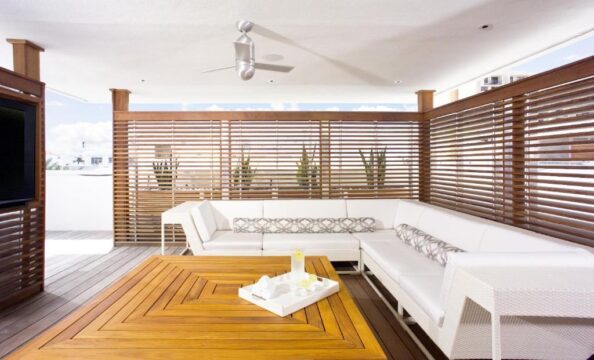 Modern outdoor living space with a large white sectional sofa, a slatted wood privacy screen, and a wooden coffee table on a deck.