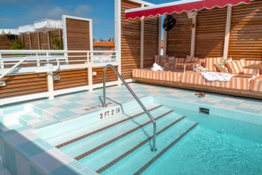 Rooftop plunge pool with steps labeled "3 FT 2 IN" and a cushioned daybed with striped cushions and a red awning, offering a luxurious sunbathing experience.