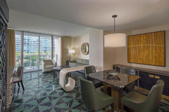 Luxurious modern living and dining room with green marble floors, contemporary furniture, and a large abstract painting. Floor-to-ceiling windows offer city views.