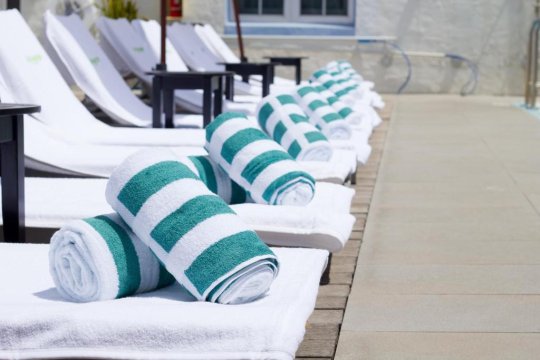 Rolled teal and white striped towels rest on white lounge chairs by a swimming pool, ready for guests at a resort.