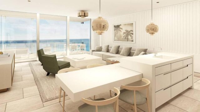Modern, bright open-plan living room with a large sectional sofa, dining table, and kitchen island, featuring floor-to-ceiling windows with ocean views.