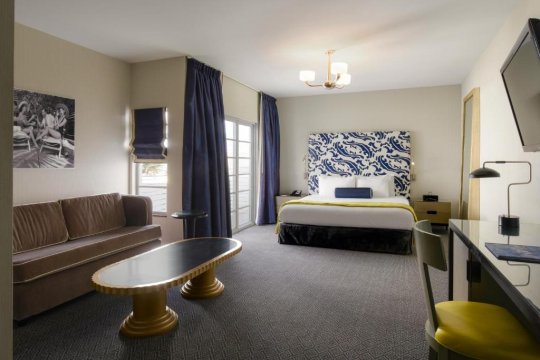 Luxurious hotel room with a king-size bed featuring a blue and white patterned headboard, a brown sofa, and a modern coffee table.