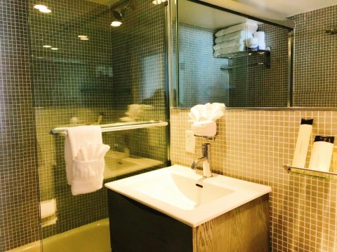 Modern hotel bathroom with a tiled shower, sink, and vanity. White towels are neatly folded on a rack next to the sink.
