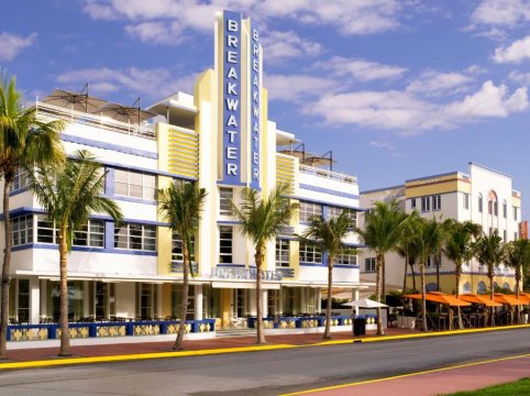 Art Deco Breakwater hotel in Miami Beach, Florida, with blue and yellow accents, palm trees, and sunny skies.
