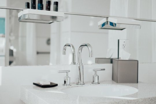 Modern bathroom sink with a sleek chrome faucet, white countertop, and a dispenser of facial tissues next to a bar of soap.