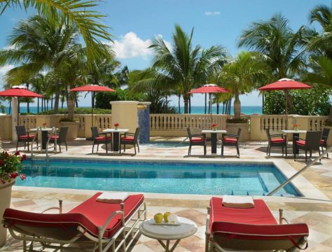 A luxurious poolside scene with lounge chairs and umbrellas, overlooking the ocean and palm trees. This tropical resort setting offers a relaxing vacation experience.