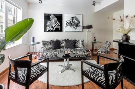 A chic living room with zebra print sofa and chairs, featuring abstract zebra art and a large green plant.