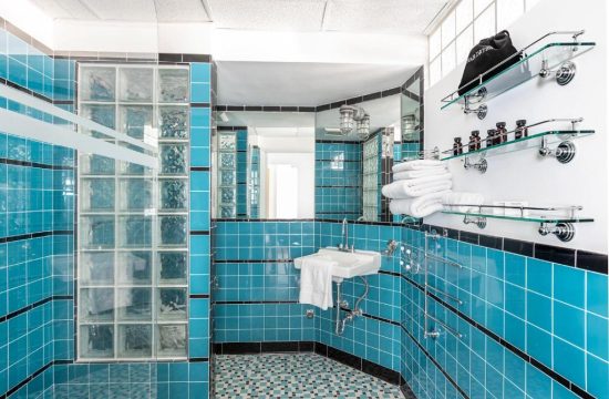 A vibrant blue tiled bathroom with a glass block shower, sink, and shelves stocked with toiletries and towels.