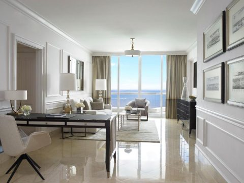 Luxurious hotel suite living room with ocean view. Features a modern desk, comfortable seating, and elegant decor, perfect for a luxury travel blog.
