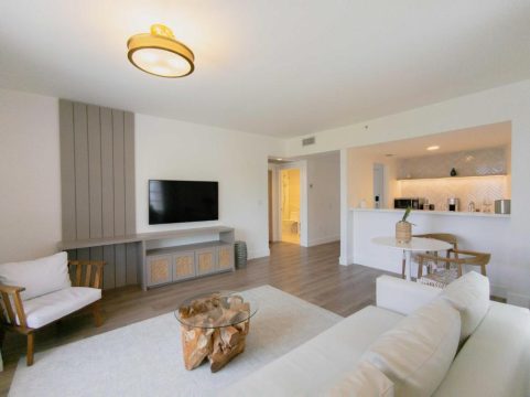 Bright and airy modern living room with a white sectional sofa, a wooden coffee table, and a wall-mounted TV on a grey media console.