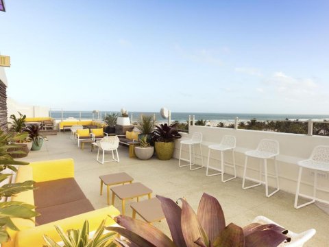 Rooftop patio with white bar stools, yellow seating, and ocean views, ideal for outdoor entertaining and relaxation.