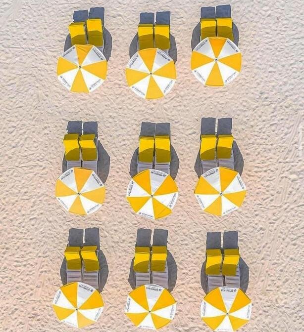 Aerial view of a pristine beach with rows of yellow lounge chairs and open yellow and white umbrellas, ready for a relaxing day at the resort.