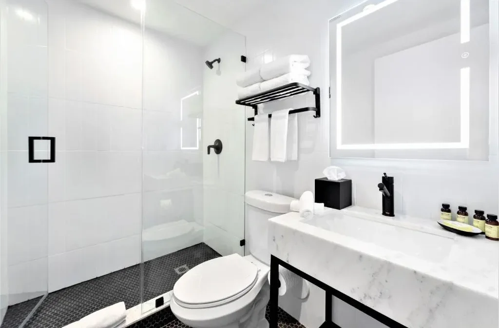 Modern white bathroom with a sleek glass-enclosed shower, marble vanity with a black faucet, and a well-lit mirror.
